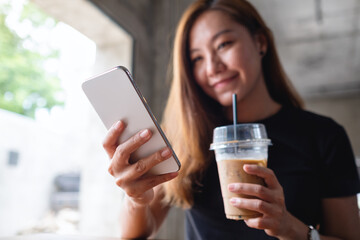 Closeup image of a beautiful young asian woman holding and using mobile phone while drinking coffee in cafe