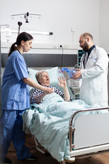 Medical team helping senior woman patient laying in hospital bed, to breath with espiratory mask with resuscitator for ventilation of patient, during cardiopulmonary resuscitation process.