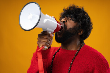 Young african american man in red hoodie screaming in megaphone against yellow background