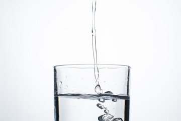 Jet of water or alcohol is pouring into a glass with splashes and bubbles, copy space