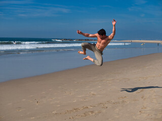 Excited shirtless young man jumping on beach