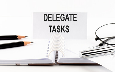 Text DELEGATE TASKS on paper card,pen, pencils, glasses,financial documentation on table - business concept