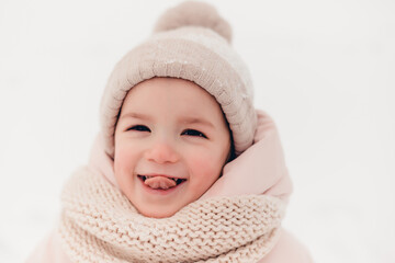 Happy laughing girl wearing a pink jacket, scarf and hat, playing in a beautiful snowy winter walk. Girl enjoys winter, frosty day. Playing with snow on winter holidays. Winter holidays concept.
