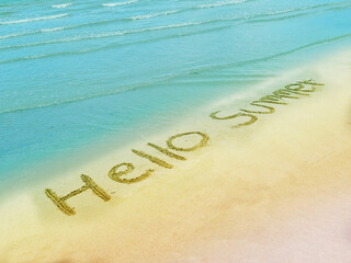 Handwritten hello summer message on sandy beach and clear sea