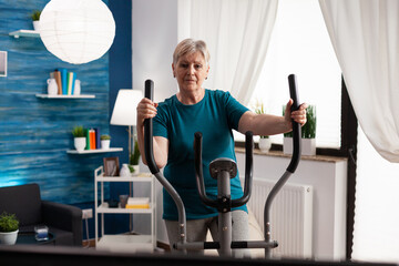 Active retirement senior woman working legs muscle using cycling bicycle machine watching fitness...