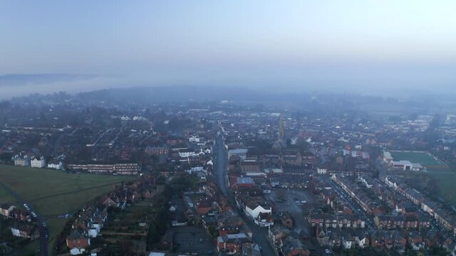 An aerial shot flying above an English town in Surrey on a misty morning.