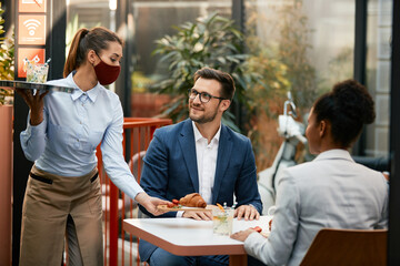 Waitress with protective face mask serving guests in a restaurant.
