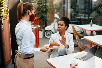 African American businesswoman discussing with waitress and rejecting the food she is serving to...
