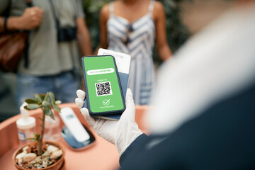 Close-up of hotel receptionist checking guest's COVID-19 vaccination passport on mobile app.