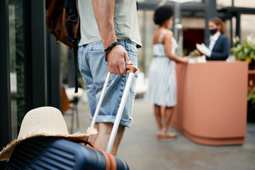 Unrecognizable man with suitcase entering in hotel while being on vacation during coronavirus pandemic.