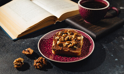 a sandwich with chocolate paste, a cup of coffee and an open book on a dark background
