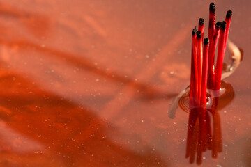 Burnt out old incense sticks in red water at a Burmese temple in Thailand