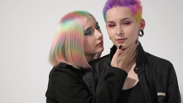Young lesbian woman couple with vivd colored short hair and jackets posing on white background. Piercing on the face, tunnels in the ears. The concept of same-sex wedding.