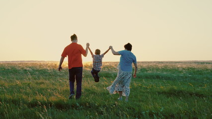 Dad, son, mom, play together run, happy child holds hands of parents, child is jumping on green grass. Family walk in park in spring at sunset, healthy childhood. Family weekend in summer in nature