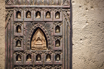 Buddhist wooden carving on a yellow plaster wall with copy space religious artifacts with light from above casting shadows temple art