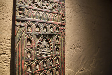 Buddhist wooden carving on a yellow plaster wall with copy space religious artifacts with light from above casting shadows temple art