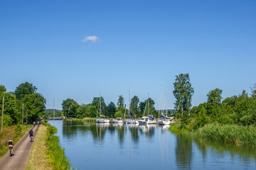 Obraz premium Cyclists on a road at a canal with boats