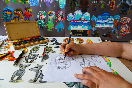 The animator draws with a pencil and draws characters from cartoons, comics or puppet shows. Mowgli's play. Preparing to make a doll. The designer creates sketches. Comics, cartoons, puppet theater