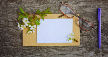 Spring memories. Bunch of cherry flowers on wooden background and over a piece of paper. Glasses and ballpen beside. Spring background.