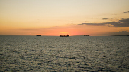 Naklejka na ściany i meble Sunset in the sea with view of tanker vessel on the horizon line
