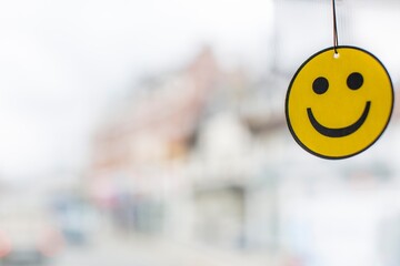 Happy Face Car Air Freshener with large copy space on the left yellow and black smiling face hanging with a blurred white and mixed colour background