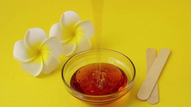 Depilatory sugar paste with Frangipani (plumeria) flowers and wooden shugaring spatulas on a yellow background. Epilation, depilation, hair removal, beauty. Place for text. Background.