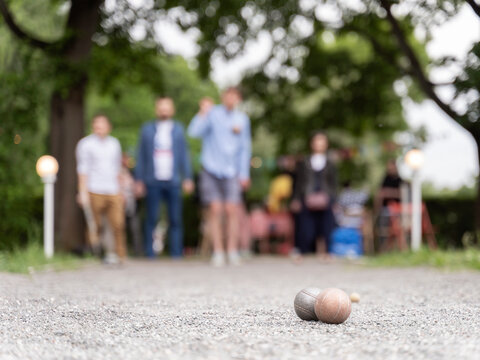 Friends playing petanque in city park on bocce court guy through a ball