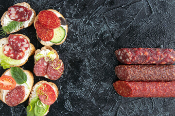 top view on six sandwiches or snacks with sausages and three kinds of different sausages on a black...