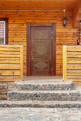 Front door and porch with stone paved steps in log house. Lantern next to the door. Vertical image.