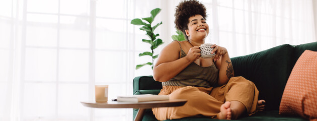 Smiling woman sitting on sofa having coffee