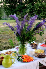 Midsummer food table.Table filled with drinks and food outside in the garden under the trees. on the table a glass vase with blue meadow flowers. Latvian LIGO festive
