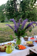 Midsummer food table.Table filled with drinks and food outside in the garden under the trees. on the table a glass vase with blue meadow flowers. Latvian LIGO festive