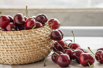 berries of ripe red sweet cherries in a wicker bowl and poured on the table, cherry harvest, summer berry still life background