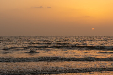 Obraz premium A view of the orange glow in the sky with sun setting in the horizon and waves in the ocean 