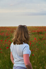 Naklejka na ściany i meble Happy young woman in field of poppies from back at sunset. Concept freedom, happiness, calm and summer vacation.