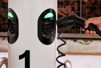 Close up of hand holding charging device, plugging into charging point station of car sharing...