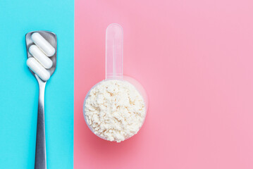 Protein scoop and capsules on pink and blue background close-up, copy space.