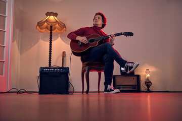 Male musician playing acoustic guitar on the amplifier in retro vintage room.