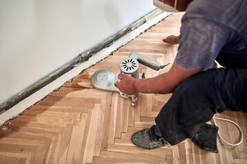 Repairman restoring parquet with a sanding machine.