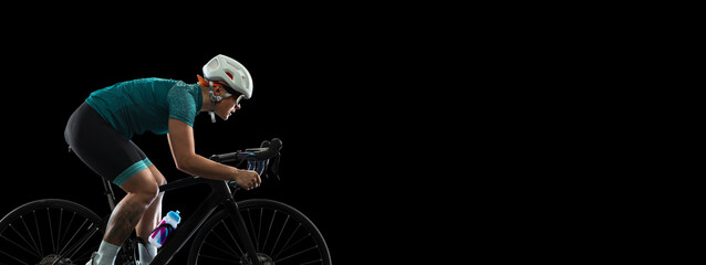 Professional young female cycler on road bike isolated over black studio background.