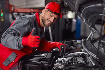 Fototapeta na wymiar Cheerful mechanic showing thumb up while repairing car engine
