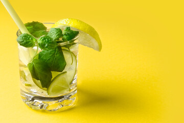 Citrus water with lemon, lime and mint. A glass of lemonade on a yellow background. Vitamin drink. Healthy diet. Concept..