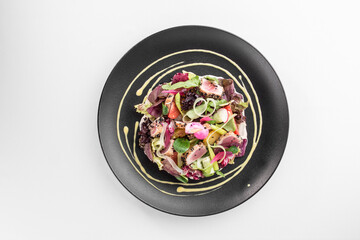 healthy green salad with seared tuna and orange on black plate isolated on white background