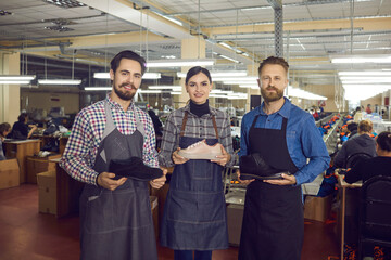 Skilled professional shoemaker colleague team holding leather shoes posing for camera with satisfied smile. New fashion footwear collection presentation. Shoes for every occasion. Factory industry