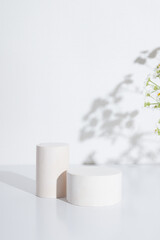 Empty cylindrical podium or pedestal with chamomile flowers on a white background. Blank shelf...