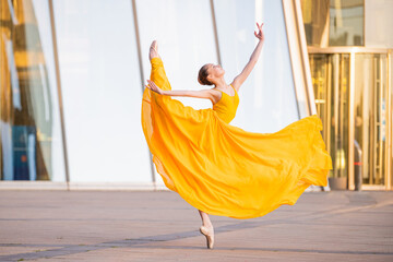 young ballerina in a long flying yellow dress is dancing against the backdrop of cityscape - Powered by Adobe