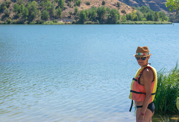 woman in hat and life jacket standing by the river