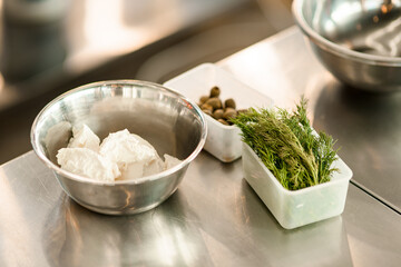 close-up of bowl with soft cheese and box of dill herbs on the table