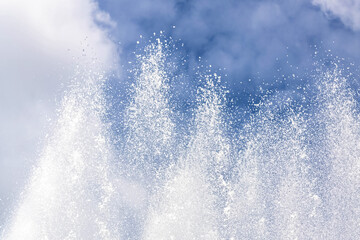 Background of water jets and fountain splashes against a blue sky with clouds
