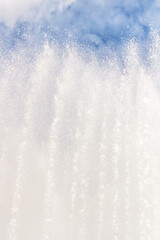 Background of water jets and fountain splashes against a blue sky with clouds